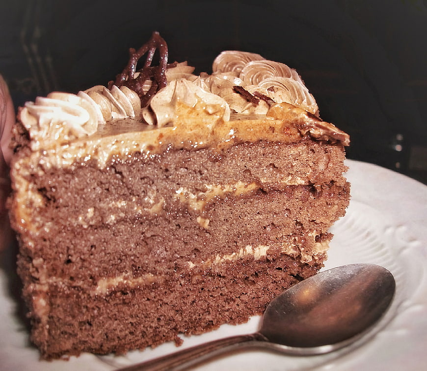 Slice of layered chocolate cake with caramel frosting and spoon