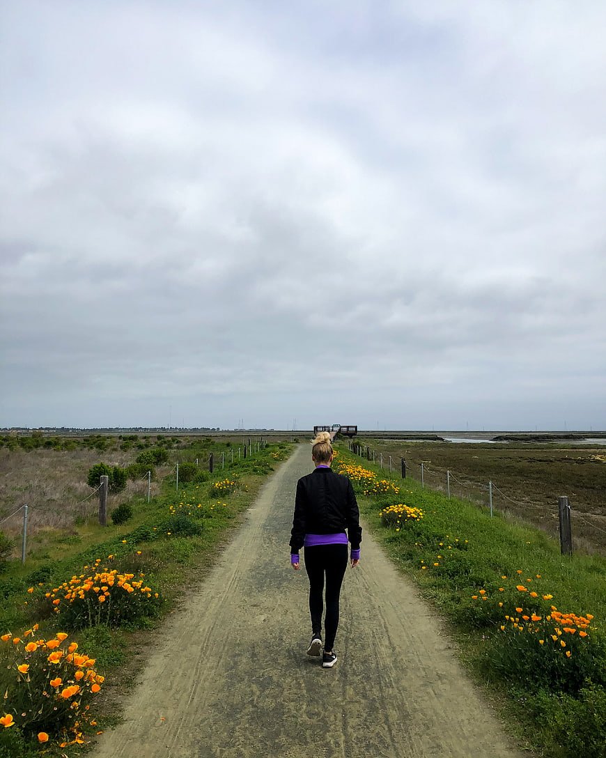 Woman walking away on dirt path with wildflowers