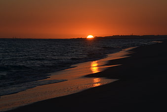 Vibrant Orange Sunset Over Ocean Beach with Silhouette