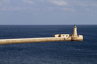 Lighthouse on stone pier extending into deep blue sea