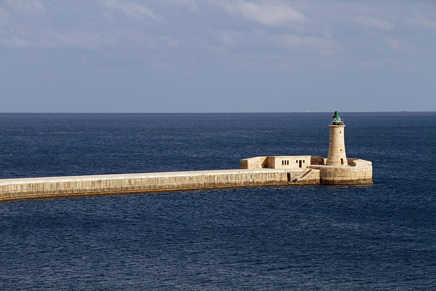 Lighthouse on stone pier extending into deep blue sea