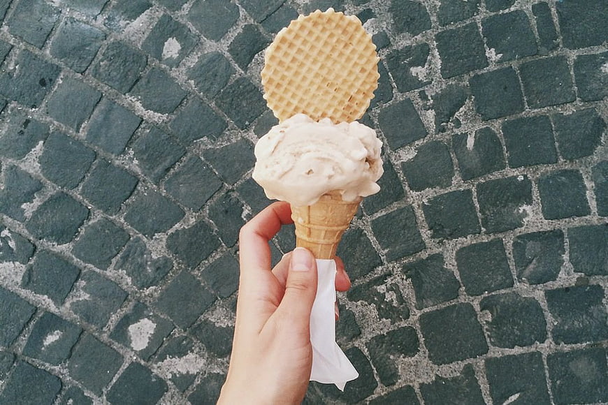 Hand Holding Ice Cream Cone on Cobblestone Street