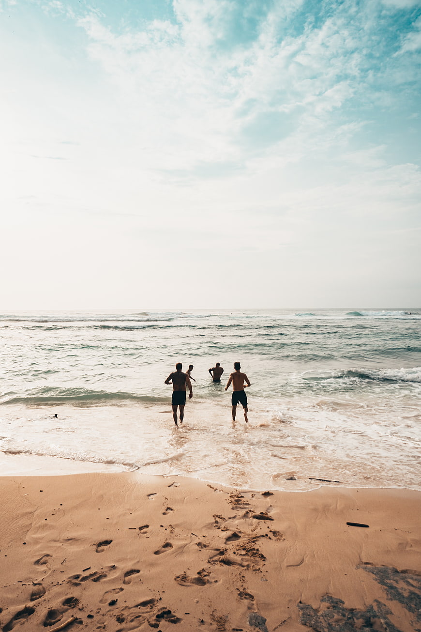 Friends Running into Ocean Waves on Sandy Beach