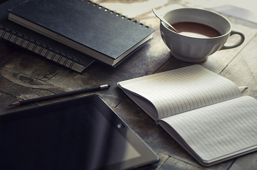 Cozy workspace with coffee, notebooks, and tablet on wooden desk