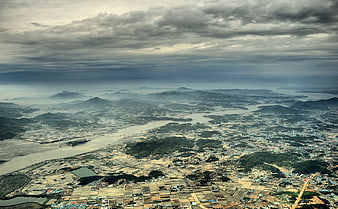 Aerial View of Coastal City, River Delta, and Mountains Under Cloudy Sky