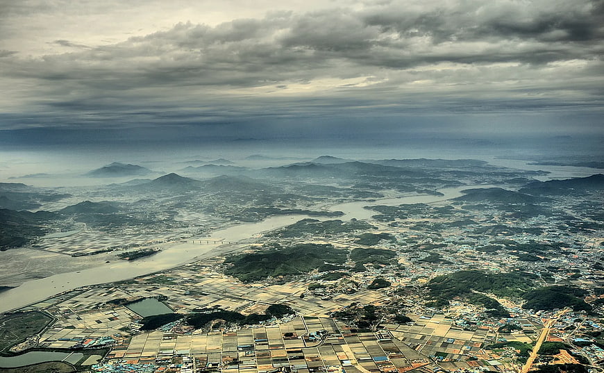 Aerial View of Coastal City, River Delta, and Mountains Under Cloudy Sky