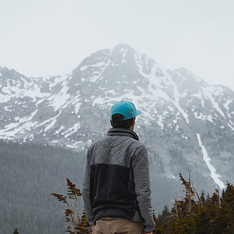 Man in Blue Cap Looking at Snowy Mountain Peak