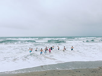 Group of friends running into ocean waves on beach
