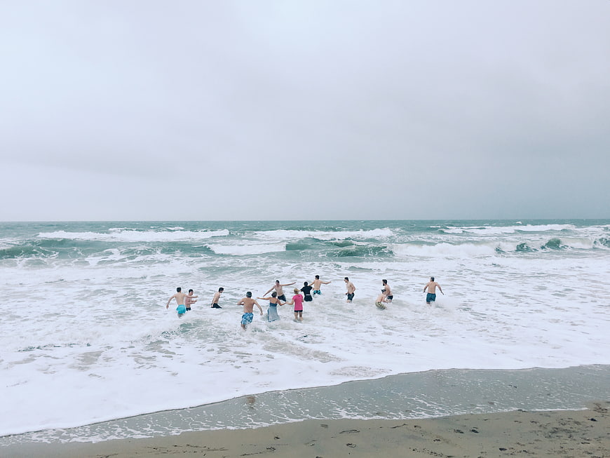 Group of friends running into ocean waves on beach