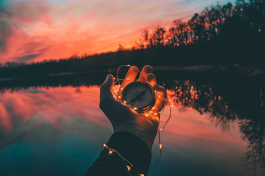 Hand holding compass with fairy lights at sunset