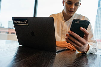 Young man multitasking with laptop and smartphone in modern office
