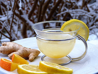 Glass cup of ginger lemon tea with citrus slices on snowy background