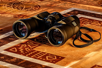 Black binoculars on patterned rug with warm lighting