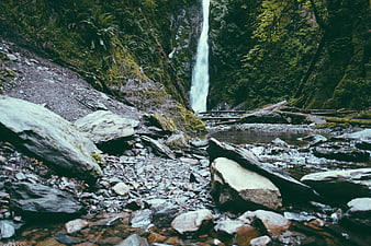 Tall waterfall cascading into rocky stream in lush green forest