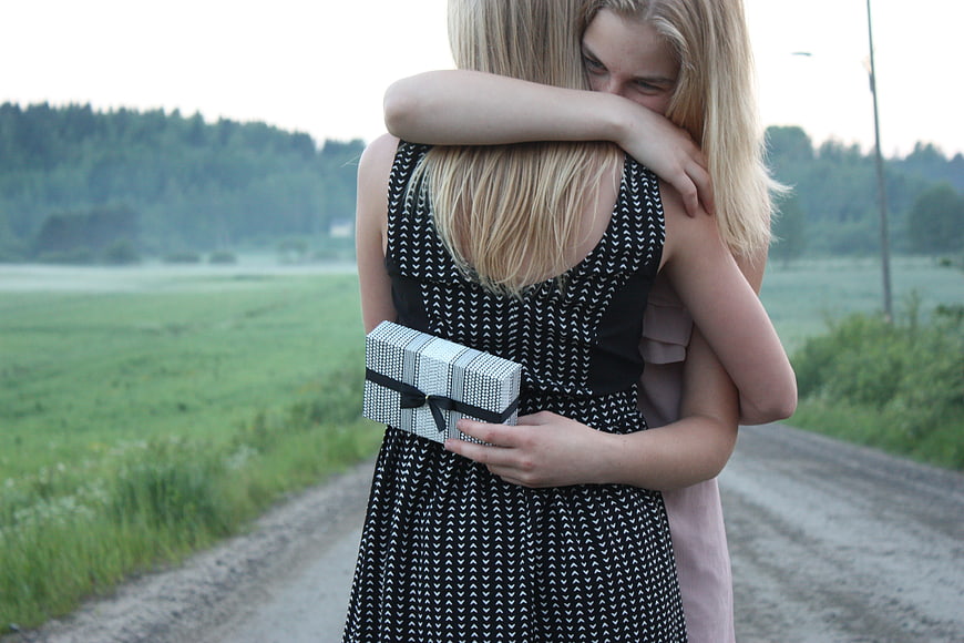 Two women hugging on a country road with a gift box