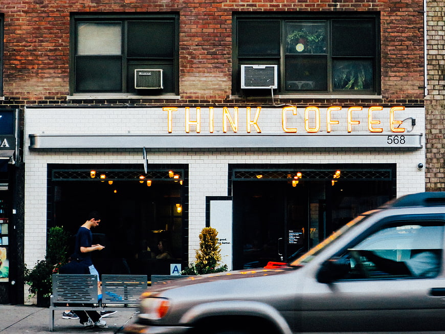 Urban street scene with Think Coffee shop and passing car
