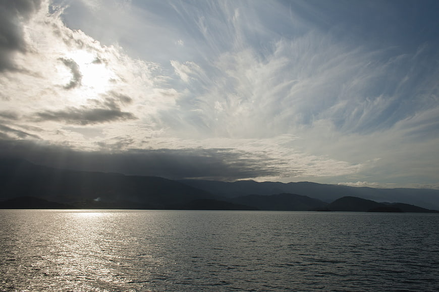 Dramatic Sun Rays Over Calm Sea and Mountains