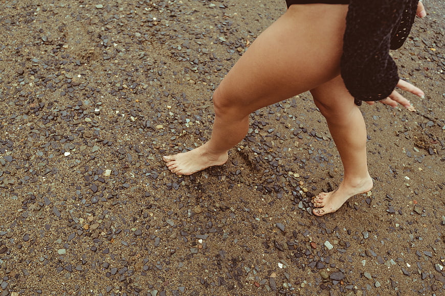 Barefoot woman walking on pebbly beach terrain