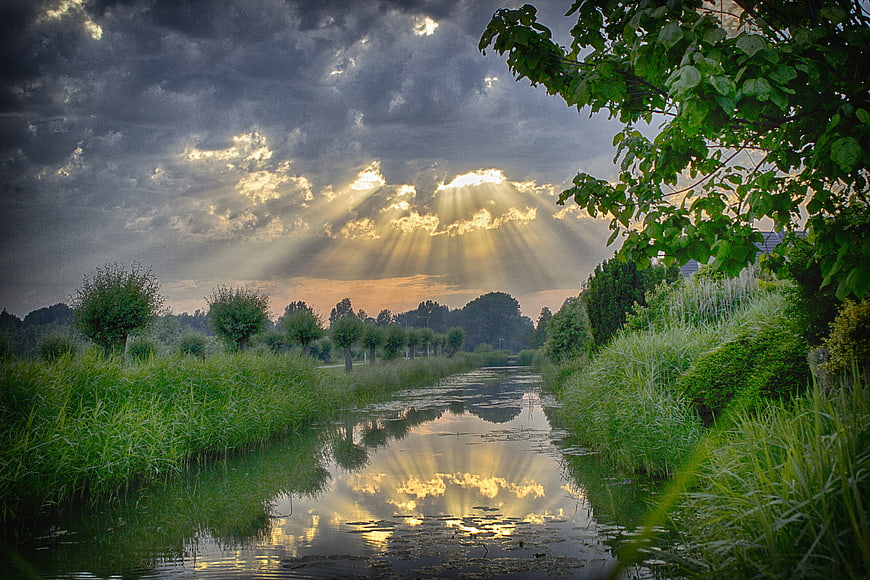 Dramatic sun rays breaking through storm clouds over a canal