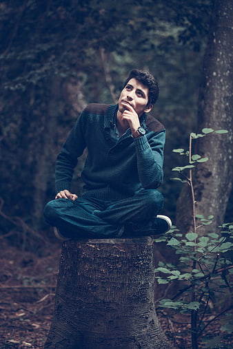 Thoughtful young man sitting on tree stump in forest