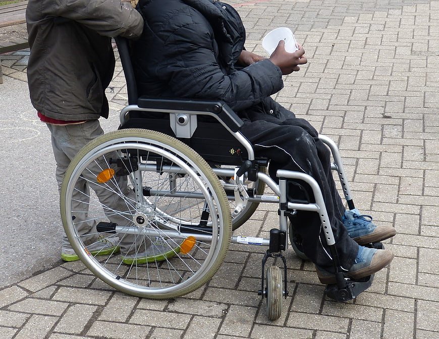 Child Pushing Person in Wheelchair on Paved Path