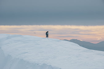 Lone hiker on snowy mountain ridge at sunset