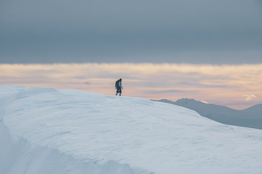 Lone hiker on snowy mountain ridge at sunset