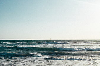 Serene Ocean Waves with Distant Sailboat on Sunny Day