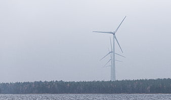 Wind turbines in foggy landscape with forest and water