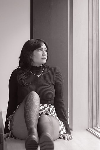 Black and white portrait of woman with tattoos sitting by window