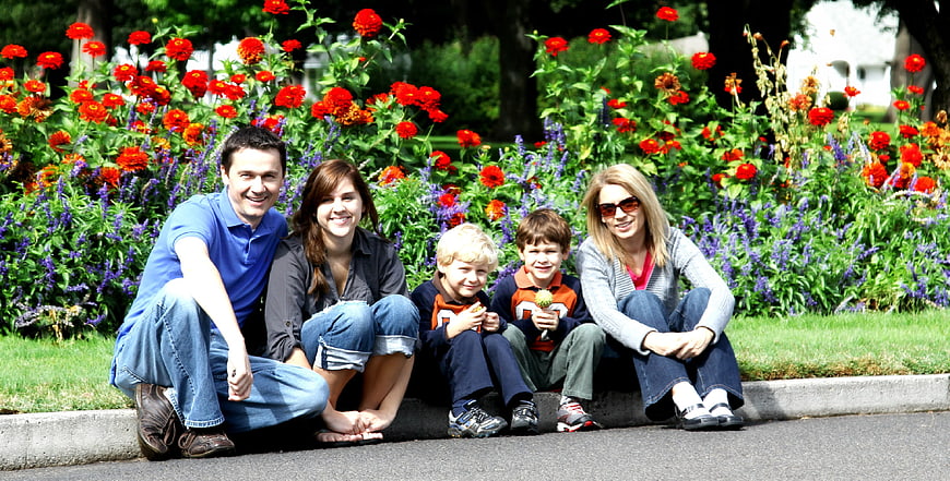 Happy family of five sitting on curb in front of flower garden