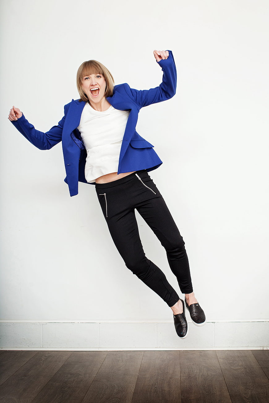 Excited woman jumping in blue blazer against white background