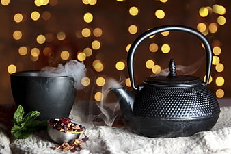 Steaming black cast iron teapot with herbal tea and mint