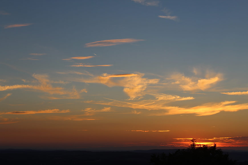 Golden sunset sky with wispy clouds over dark mountain silhouette