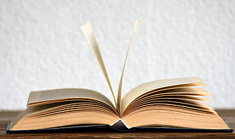 Open book with pages fluttering in wind on wooden table