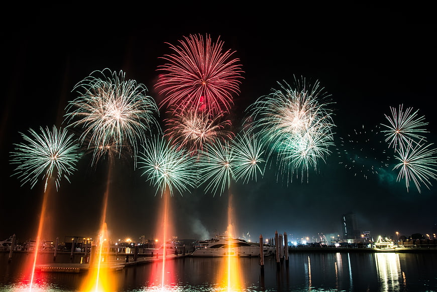 Colorful fireworks exploding over marina with boats at night