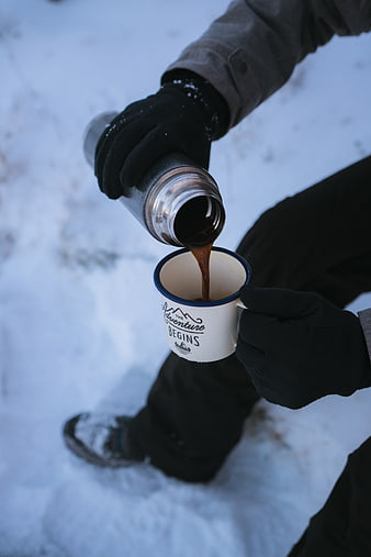 Pouring hot coffee from thermos into mug in snowy winter landscape