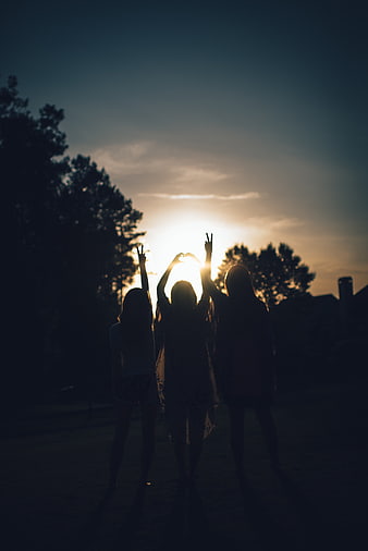 Silhouette of Three Friends Making Peace Signs at Sunset