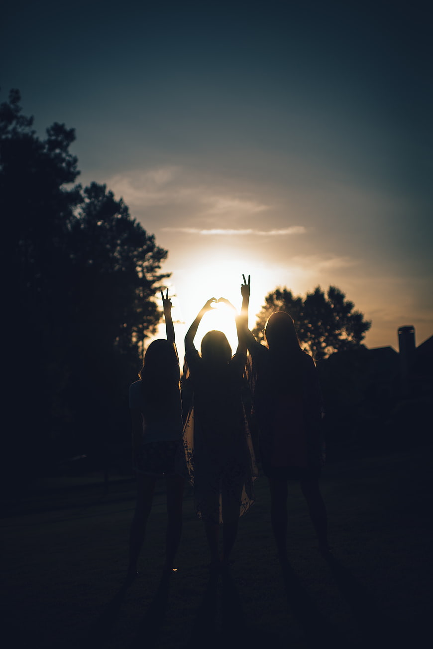 Silhouette of Three Friends Making Peace Signs at Sunset