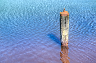 Rusty wooden bollard standing in calm blue water