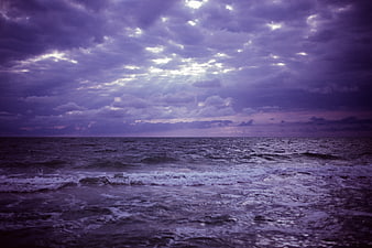 Dramatic purple stormy ocean waves under cloudy sky