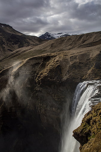 Dramatic waterfall cascading down mossy cliffs in rugged mountains
