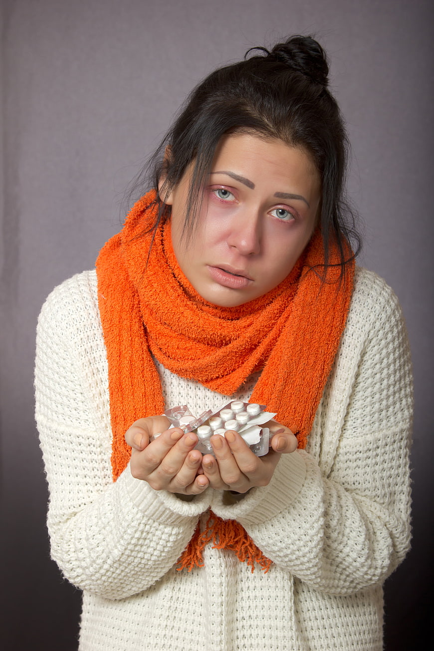 Sick young woman with red eyes holding pills and scarf