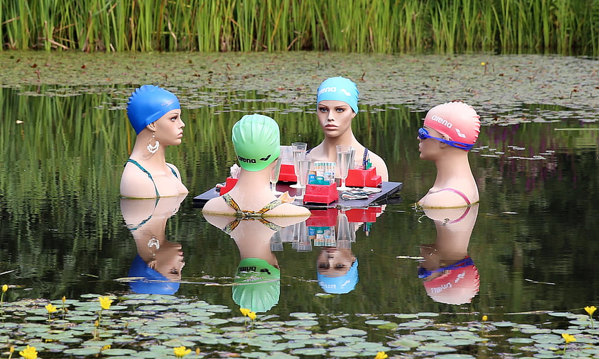 Four Mannequins Wearing Swim Caps Seated at Table in Pond