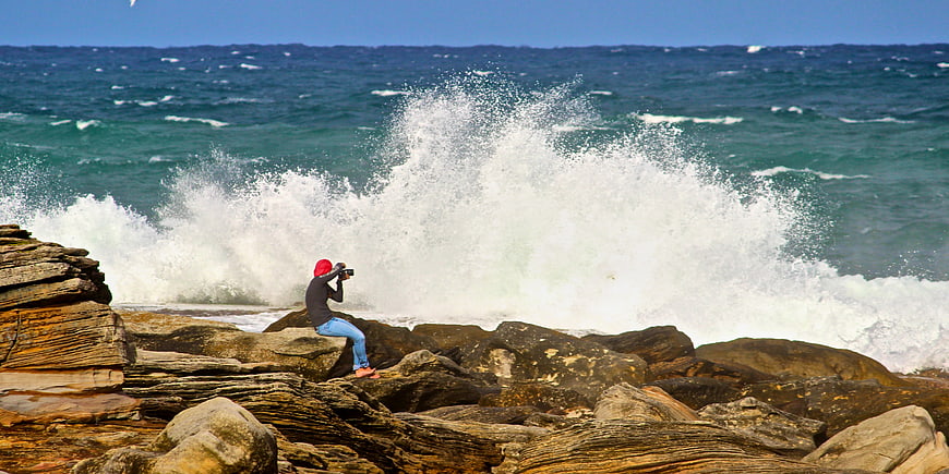 Photographer capturing crashing waves on rocky coastline