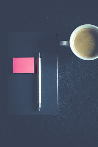 Minimalist flat lay of notebook, pen, sticky note, and coffee cup on dark desk