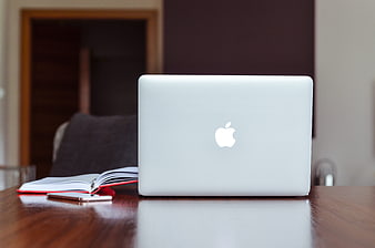 Silver MacBook laptop on wooden desk with notebook and smartphone