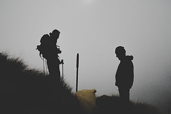 Silhouettes of two hikers on a foggy mountain ridge