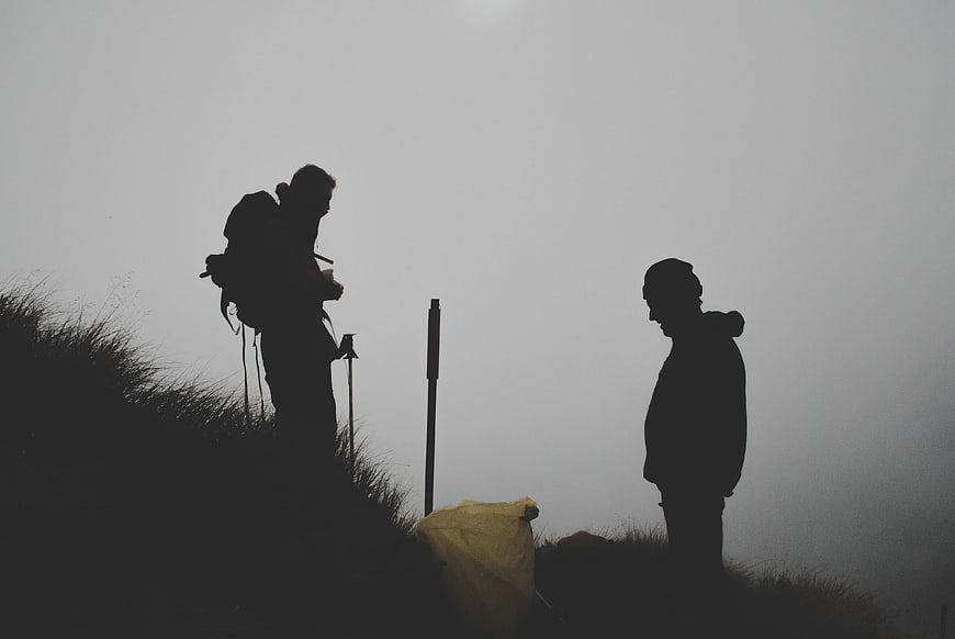 Silhouettes of two hikers on a foggy mountain ridge