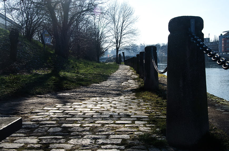 Cobblestone path along riverbank with bollards and chains